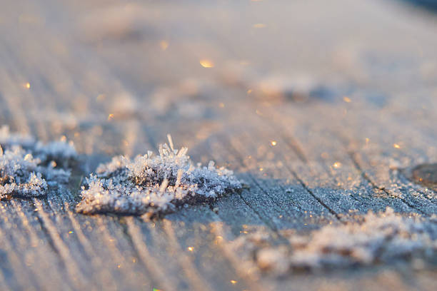 Macro shot of frost crystals in morning sunlight, sharp detail on small ice mound, soft blurred background with bokeh circles, natural abstract winter texture, cold season atmosphere, minimal beauty.