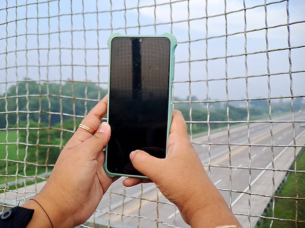istock Person using a mobile phone on a bridge overlooking a highway, capturing distance and perspective. 2244722544