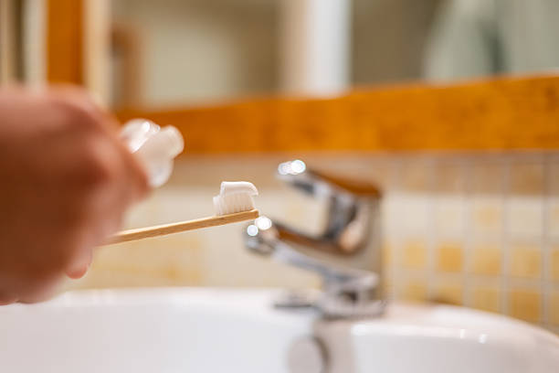 istock Person squeezing white toothpaste onto a natural bamboo toothbrush over a sink, preparing for daily oral hygiene, promoting sustainable living and environmentally conscious dental care routine 2244724860