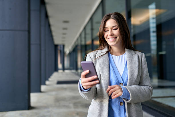 istock Young happy woman using mobile phone standing outside office building. 2244726979