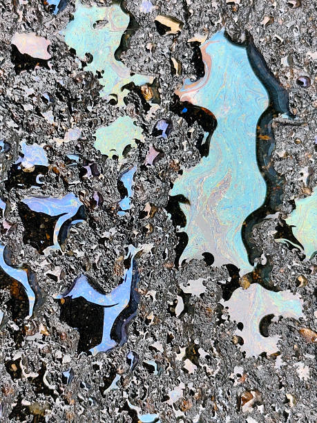 Colorful oil slick on wet asphalt creating rainbow reflections and iridescent patterns in puddles after rain.