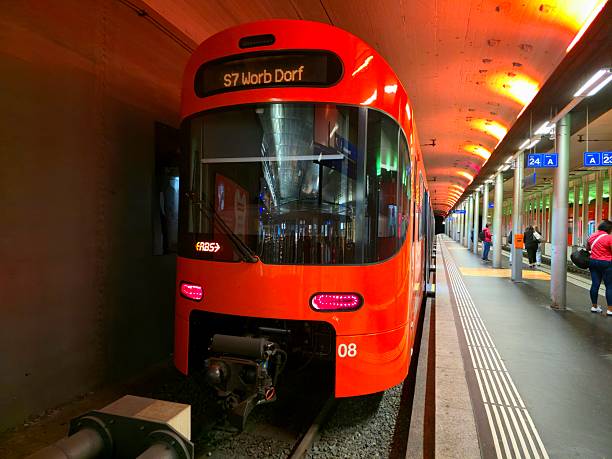 Underground station at Bern railway station (RBS). The image shows the platform and a train of RBS Railways with some people.