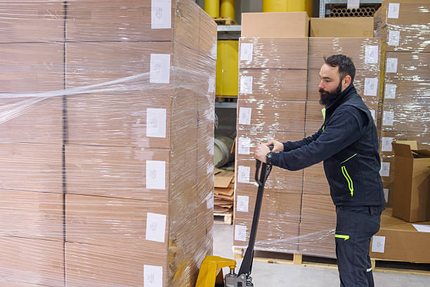 istock Man using pallet jack and moving stacked goods in the warehouse 2244732077