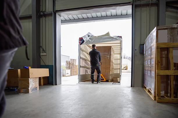 istock Man unloading truck with pallet of stacked cardboard boxes, using pallet jack 2244732837