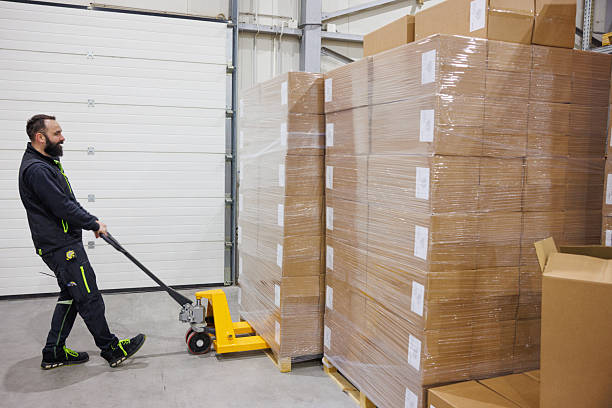 istock Man using pallet jack by the stacked goods in warehouse 2244732849