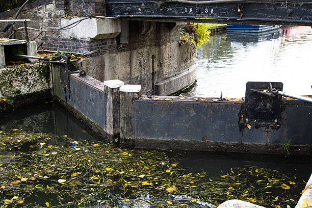 Close-up of Rammey Marsh Lock gates on the River Lea Navigation, Enfield. Wooden gates hold back canal water on a calm British waterway.