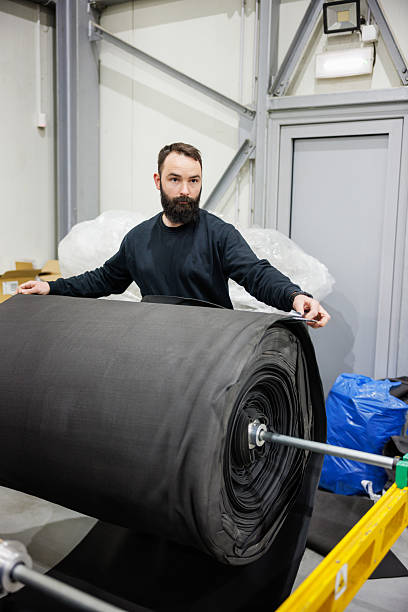 istock Worker adjusting large roll of raw material on rod in manufacturing facility 2244736297