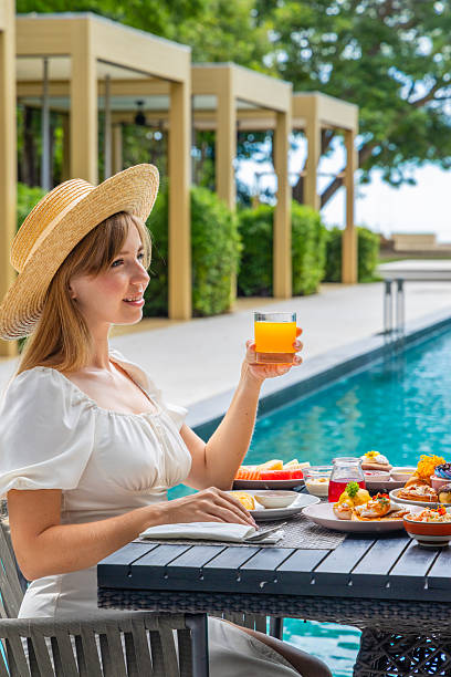 Woman enjoying tropical breakfast by poolside, holding orange juice,