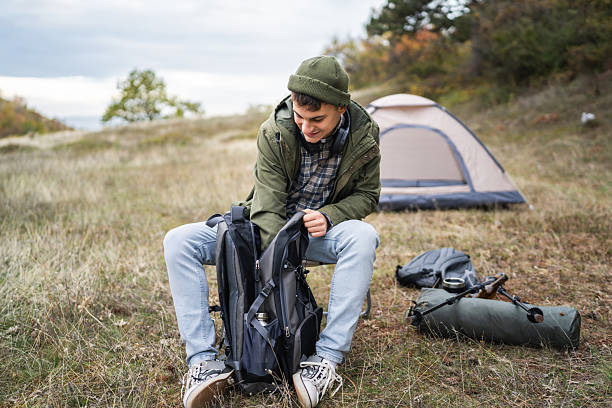 istock Young man arranging backpack gear while camping outdoors 2244743107