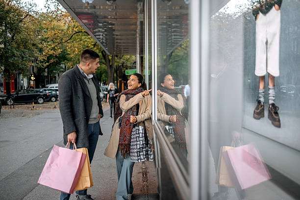 Surprised and excited young couple looking at store window and noticing the new arrivals. Shocked man accompanied by young woman while shopping.