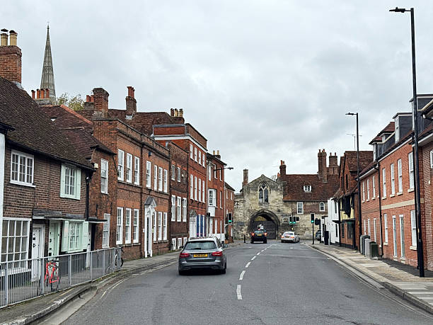 A residential street lined with red brick terraced houses on both sides, in Salisbury, Wiltshire. The houses have white window frames and door surrounds, with some having dormer windows in the roof.