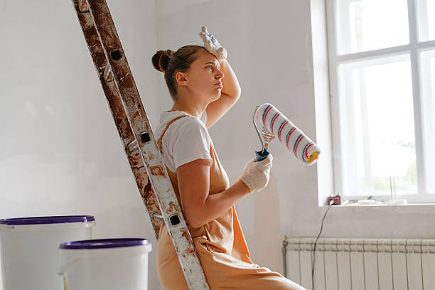 istock A woman rests on a ladder with a paint roller in hand, deep in thought, after a long day of painting a room that is bright and empty 2244761018