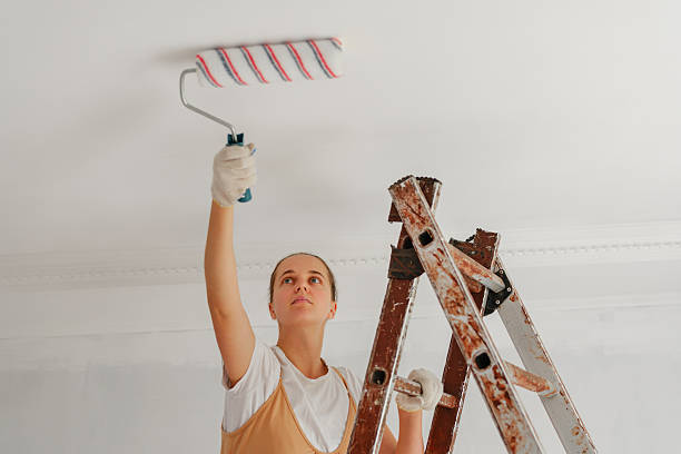 istock A woman skillfully paints the ceiling in a well-lit room using a roller, standing on a ladder to reach higher areas. She is focused on her task during the renovation 2244761027