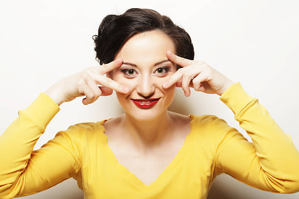 A young woman wearing a a headscarf, crop top and short shorts is having fun, grimacing and making funny face. Studio shot on pink background, top view