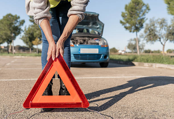 istock Woman placing reflective warning triangle on road near broken down car with open hood 2244767158