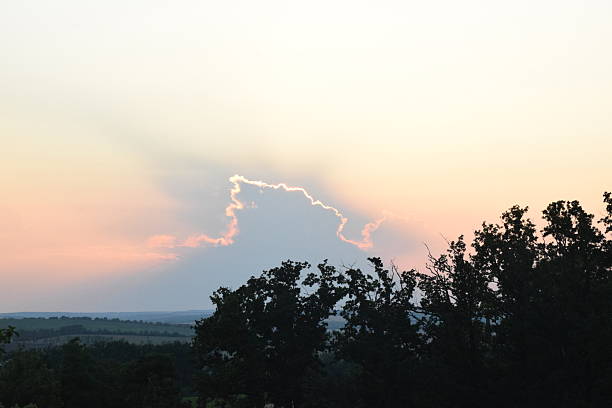 Dramatic sunset sky with vibrant colors and cloud formations, silhouetted trees in foreground, creating a serene and tranquil atmosphere for nature lovers and photographers