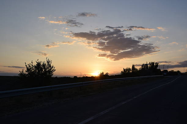 istock Sunset over a winding road, with silhouettes of trees and clouds, creating a tranquil atmosphere, inviting reflection and appreciation of nature's beauty 2244767636