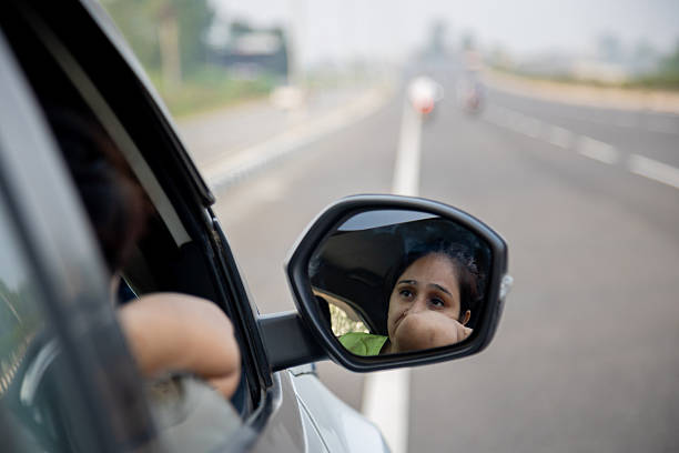 A woman driver gazes into her car’s side mirror on a busy highway. The reflection conveys focus and concern during a driving moment, emphasizing road awareness and travel.