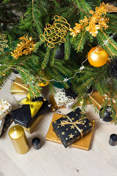 istock A festive scene featuring gold and black gift boxes, surrounded by shimmering candlelight and stylish decorations under a beautifully decorated Christmas tree, exuding elegance and charm 2244773953