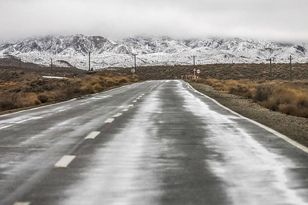 A long straight road stretching through countryside beneath dramatic clouds after rainfall. No people