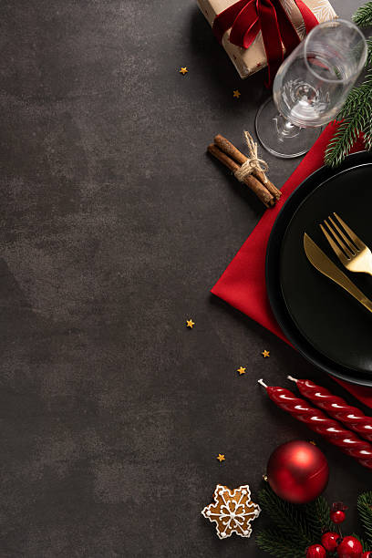istock A vertical festive holiday table scene featuring a dark backdrop, gold cutlery on a black plate, red napkin, gift box, cinnamon sticks, glass, ornament, pine branch 2244780594