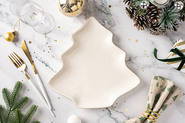 istock A festive table setting featuring a tree shaped plate, gold cutlery, pine branches, ornaments, and wrapped gifts on a marble surface, capturing holiday warmth and seasonal celebration 2244780601