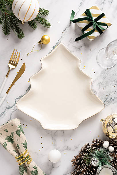 istock A vertical stylish holiday table featuring a leaf shaped ceramic plate, gold utensils, wrapped gift, ornaments, pine cones, and festive decor on a marble surface 2244780613