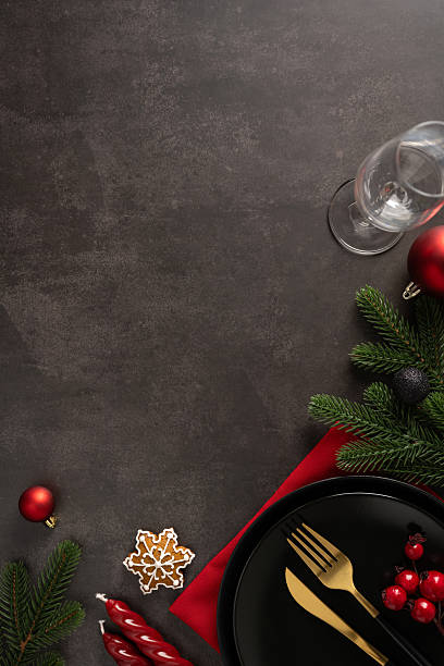 istock A dark top view vertical background frames a festive Christmas table scene with a red napkin, evergreen sprigs, red berries, a snowflake ornament, and elegant gold utensils ready for a holiday toast 2244780617