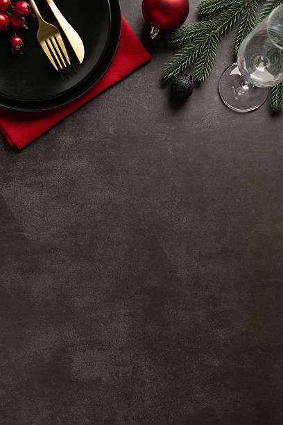 istock A vertical festive table scene with a dark surface, red napkin, black plate, gold cutlery, pine branches, berries, and a glass 2244780714
