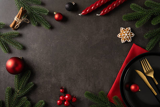 istock A warm holiday tablescape featuring pine branches, red ornaments, cinnamon sticks, a snowflake cookie, a black plate with gold cutlery, and a red napkin, perfect for Christmas and New Year greeting 2244780737