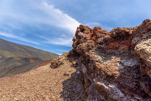 Scenic volcanic landscape with rough textured lava rocks under a bright blue sky. The image captures the raw beauty and geological formations of a volcanic mountain slope.