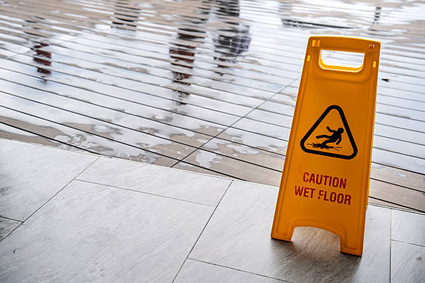 A yellow caution sign is on the ground. The sign warns people that the floor is wet. The sign is placed on a wet floor, which is likely due to rain or a spill