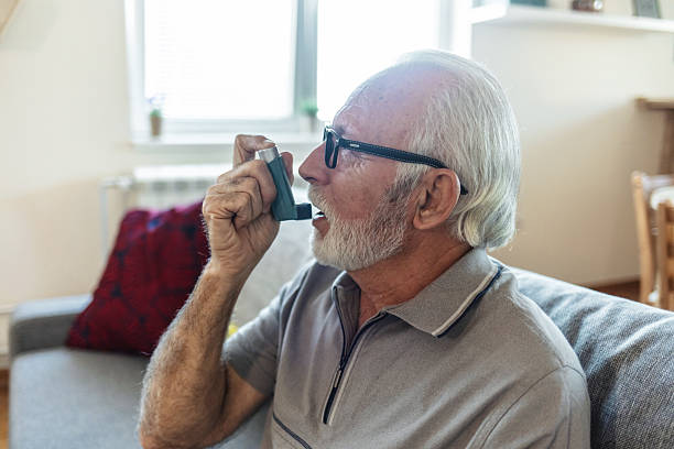 istock Senior man using asthma inhaler for relief an attack at home. Old man using asthma inhaler for preventing attack. Mature man using medical inhaler to prevent and treat wheezing and shortness of breath caused by allergy. 2244787686