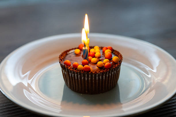 Birthday cake with white whipped cream, meringues and cranberries, decorated with multicolored lit candles. Happy Birthday concept. Tradition of making a wish blowing out candles. Selective focus.