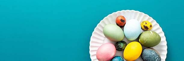 istock A beautiful assortment of Easter eggs in various colors and patterns is displayed on a round white plate against a bright blue background, perfect for holiday festivities, banner 2244789159