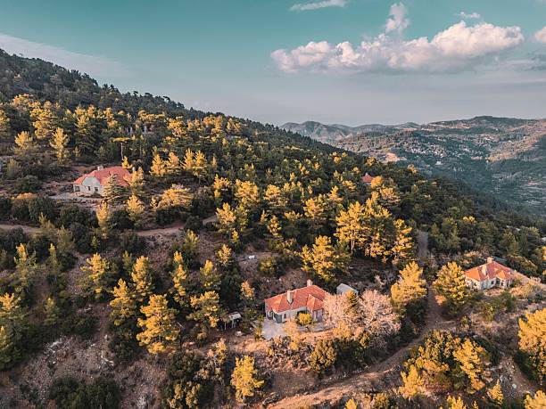 Aerial view of a scenic mountainous landscape with scattered houses and lush greenery under a partly cloudy sky.