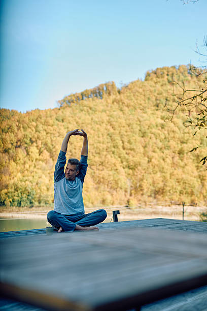 istock Man practicing yoga stretching arms on lake dock in autumn 2244795622
