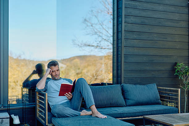 istock Man relaxing on outdoor couch reading book 2244795936