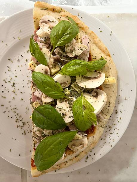 Homemade pizza slice topped with fresh mushrooms, basil leaves and dried oregano on a golden crust, showcasing Italian flavors and a savory, ready-to-eat meal
