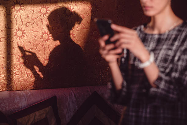 istock Dark profile shadow of a woman using a phone falls onto a patterned orange wall indoors during strong afternoon sunlight. 2244799081