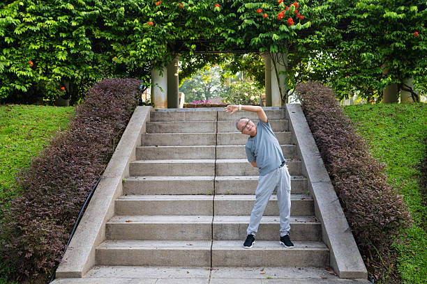 The senior Asian man engages in essential warm-up stretches before running in the park.
