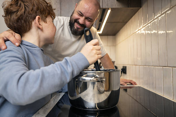 Happy cheerful young son helping his old senior father in preparing meal, food, dinner, lunch in the kitchen. Family time, cooking pasta spaghetti together. I love you, dad! Happy father`s day!