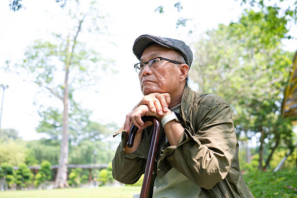 Portrait of lonely and depressed senior man in park. He is sitting on bench on autumn day.