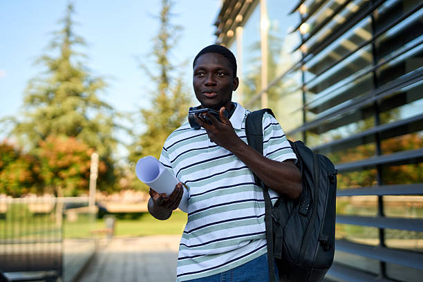 istock One black man using a mobile phone while walking outside to work and holding a roll of papers 2244808640