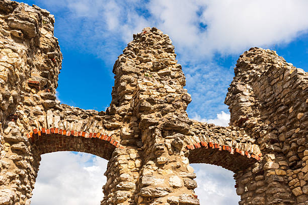 Weathered medieval stone ruins rise toward a bright sky, featuring arched windows and rugged textures. The historic structure evokes time, resilience, and architectural beauty in decay.