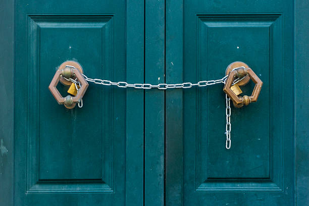 Teal double doors, secured with a metal chain and two padlocks, create a strong sense of security and a barrier. The scene evokes caution, protection, and restricted access
