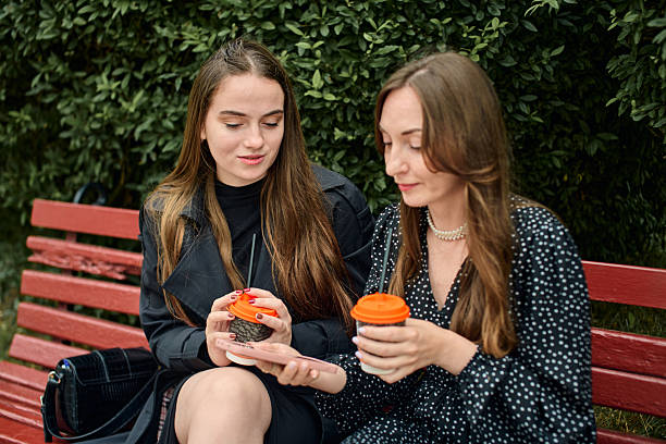 istock Young girlfriends sharing gossip over coffee on park bench with leafy background 2244819405