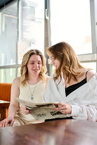 Young women reading newspaper together in bright cafe