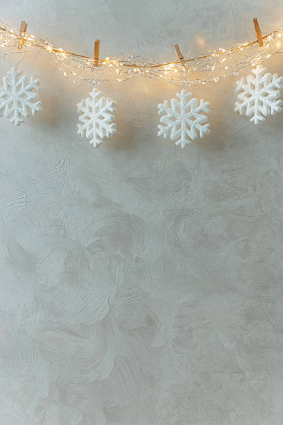 istock White Snowflake Ornaments Hanging on String Lights Against Textured Wall 2244819531