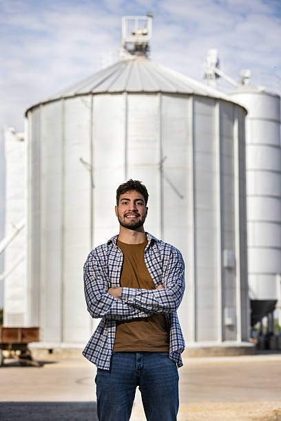istock Young worker smiling with crossed arms in front of silo 2244825007
